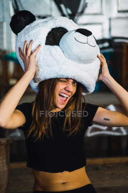 Bruna ragazza strizzando l'occhio alla fotocamera e in posa con peluche panda costume testa . — Foto stock