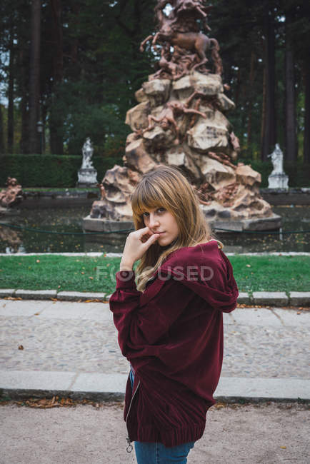Pretty brunette woman posing near statue in park. — Stock Photo