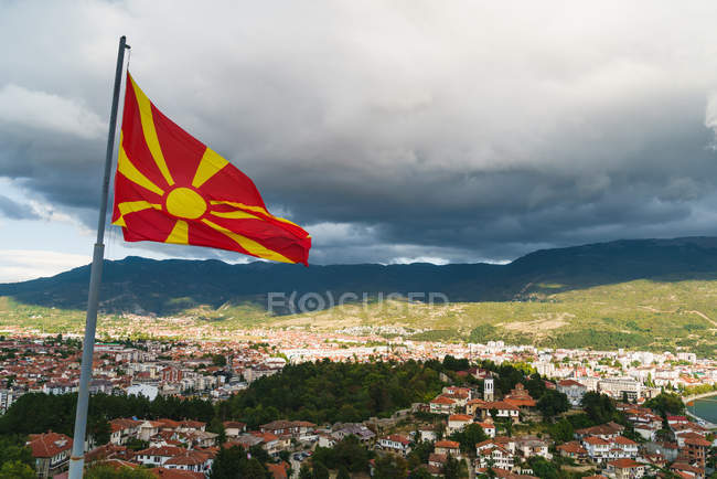 Waving flag of Macedonia on background of city placed in mountains valley. — Stock Photo