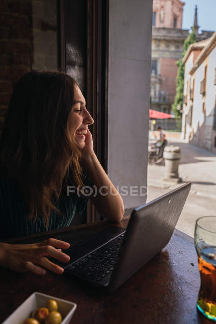 Вид сбоку смеющейся женщины на ноутбуке в кафе — стоковое фото