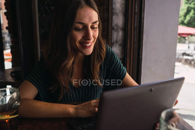 Retrato de mujer alegre mirando el ordenador portátil en la cafetería - foto de stock