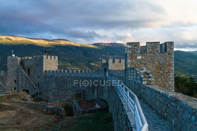 Vista da parede de pedra do castelo colocada no vale das montanhas sob o céu nublado . — Fotografia de Stock