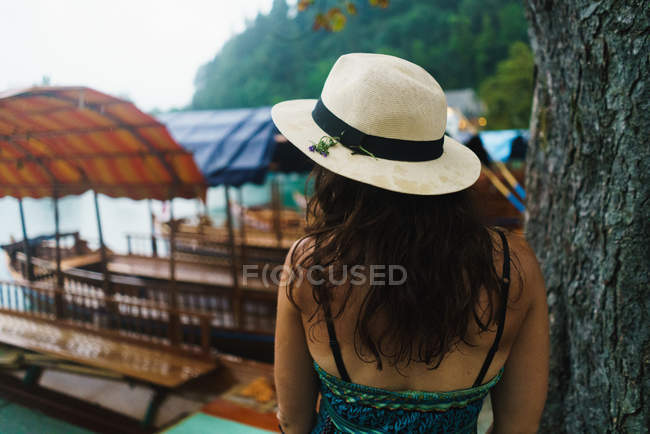Вид ззаду жінки в соломі стояв біля причальних човнів на березі озера — стокове фото