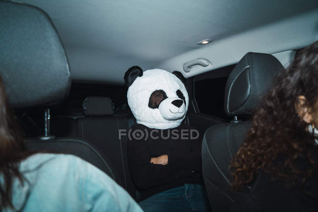 Hombre con máscara de cabeza panda sentado en el asiento trasero en el coche - foto de stock