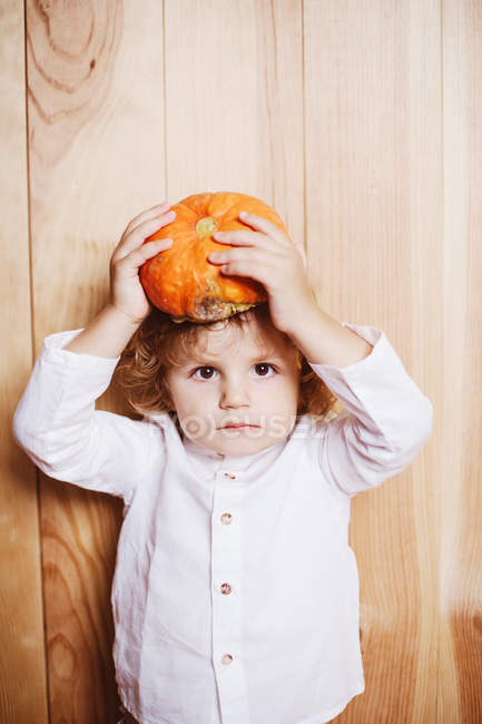 Portrait of little boy holding pumpkin above head posing at camera. — Stock Photo