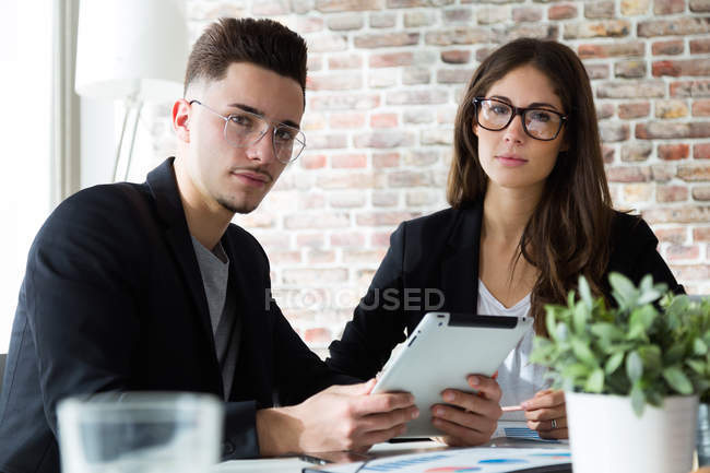 Two young colleagues sitting with tab and looking at camera in loft office. — Stock Photo