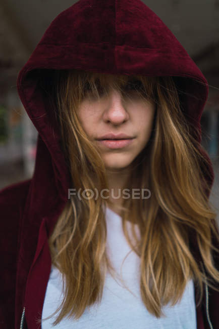 Портрет дівчини брюнетки в червоній куртці з капюшоном дивиться на камеру — стокове фото