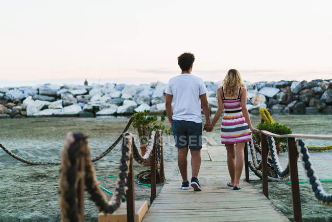 Rear view of loving couple walking on boardwalk at ocean beach — Stock Photo
