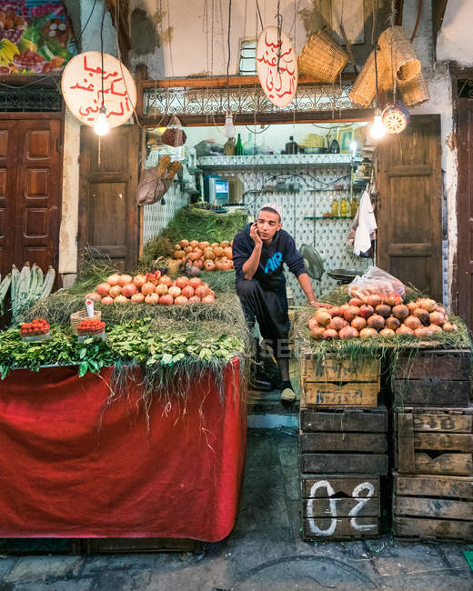 MARRUECOS - 15 DE AGOSTO: Joven vendedor cansado de pie en el mostrador con granadas y verde en el mercado . - foto de stock