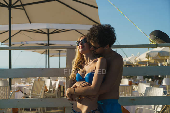 Portrait of man in sunglasses embracing girl from back on background of resort. — Stock Photo