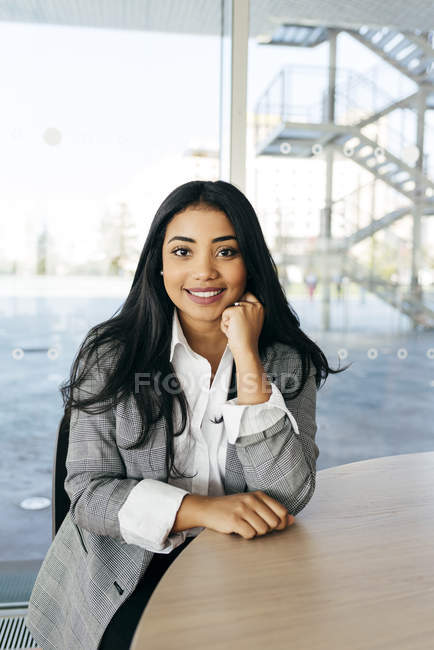 Retrato de una mujer de negocios sonriente sentada en la mesa y mirando a la cámara - foto de stock