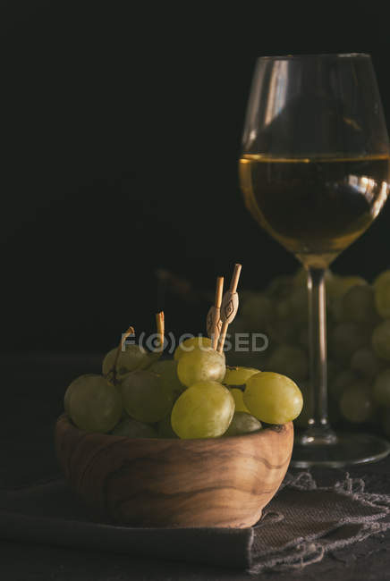 Ainda vida de ramo de uvas verdes com espetos em tigela ao lado de copo de vinho branco — Fotografia de Stock
