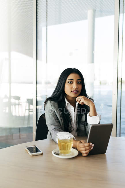 Элегантная деловая женщина сидит за столом с планшетом и смотрит в камеру — стоковое фото