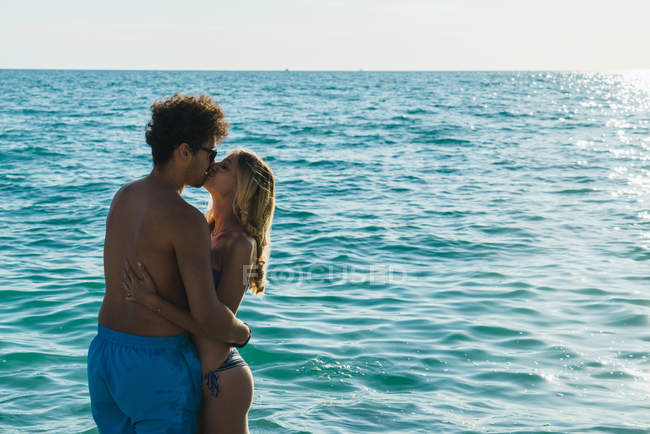 Vista lateral de pareja besándose en agua del océano - foto de stock