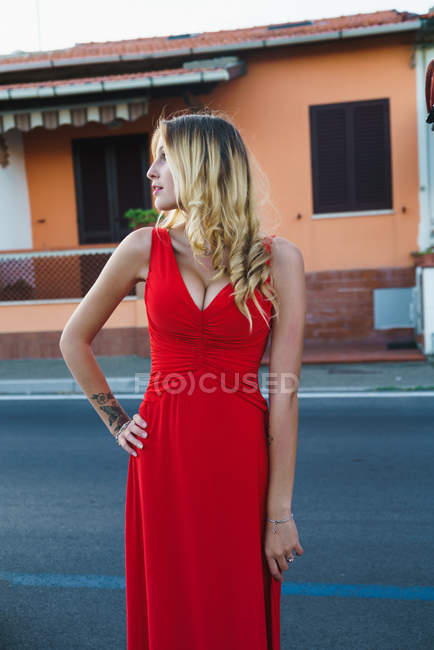 Retrato de mulher loira com penteado posando em vestido de noite vermelho na cena urbana e olhando para longe — Fotografia de Stock