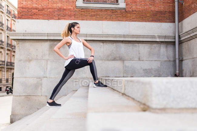 Vista lateral da menina atlética esticando as pernas nas escadas no exterior do edifício — Fotografia de Stock