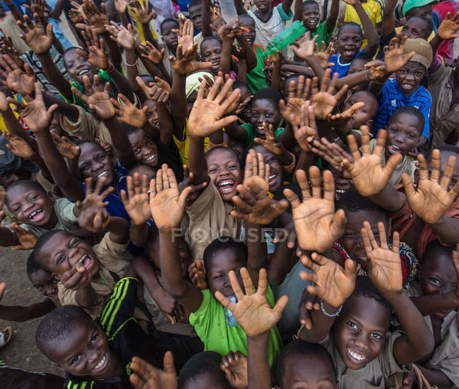 Бенин, Африка - 30 августа 2017 года: Низкий угол улыбающейся толпы черных детей жестом приветствия с поднятыми руками и глядя в камеру . — стоковое фото