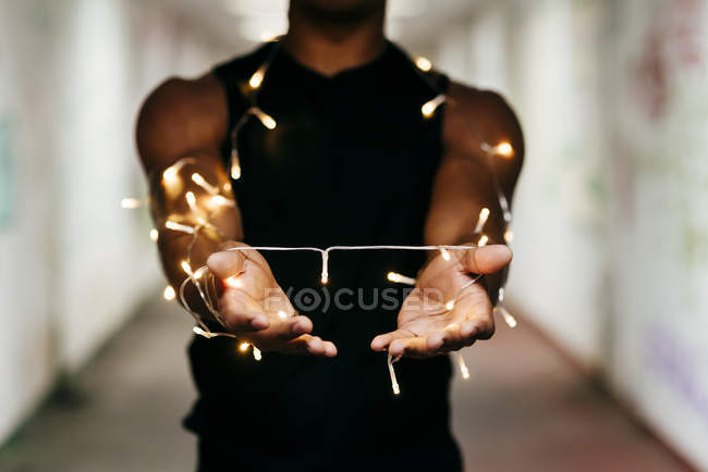 Mid section of man posing in subway with garland coiled on outstretched arms — Stock Photo
