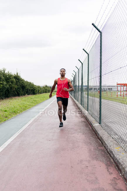Front view of man wearing headphones running along fence — Stock Photo