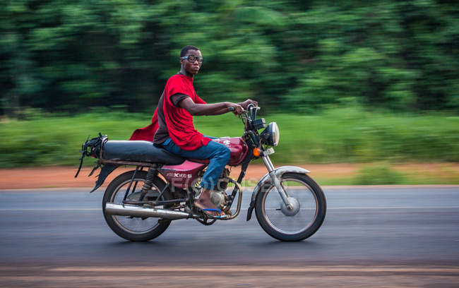 BENIN, AFRICA - AUGUST 31, 2017: Side view of man ridding on motorcycle on road — Stock Photo