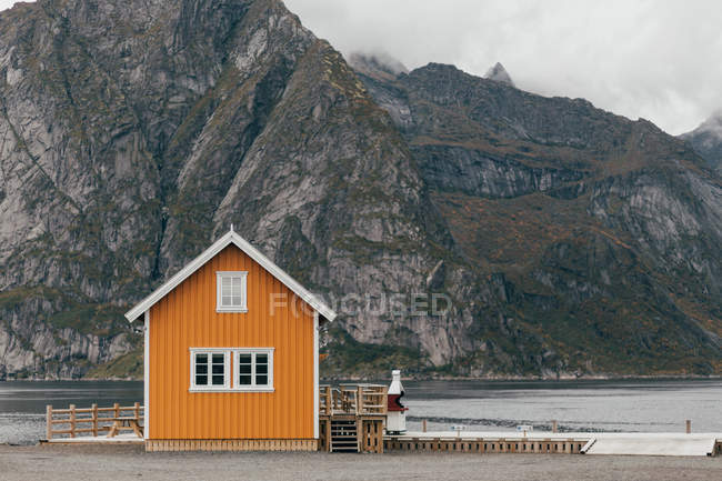 Piccola cabina in piedi sulla riva del lago sullo sfondo di massicce scogliere di montagna . — Foto stock