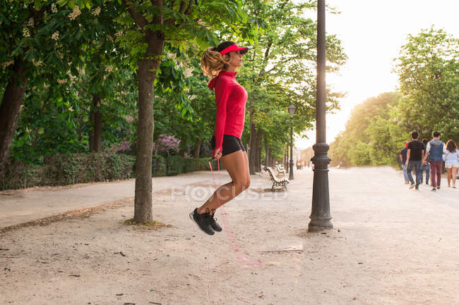 Vista lateral de niña saltando con cuerda de salto en el callejón del parque — Stock Photo