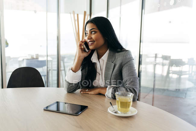 Portrait of businesswoman having phone call and sitting at table with cup of tea and tablet — Stock Photo