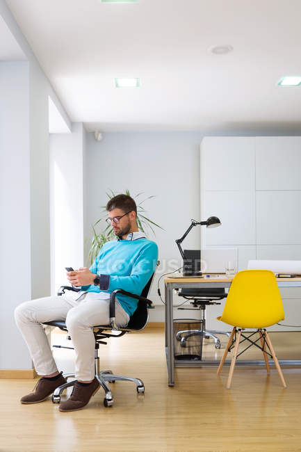 Porträt eines Geschäftsmannes, der in einem modernen Büro im Stuhl sitzt und auf seinem Smartphone surft. — Stockfoto