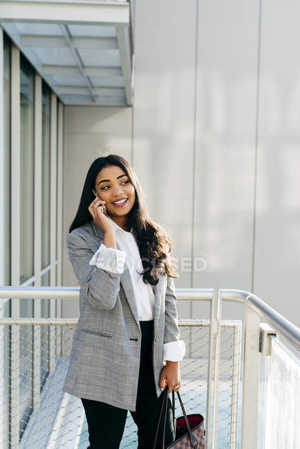 Empresária sorridente em jaqueta elegante falando no smartphone na varanda . — Fotografia de Stock