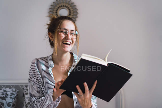 Retrato de morena riendo en gafas sosteniendo libro en las manos - foto de stock