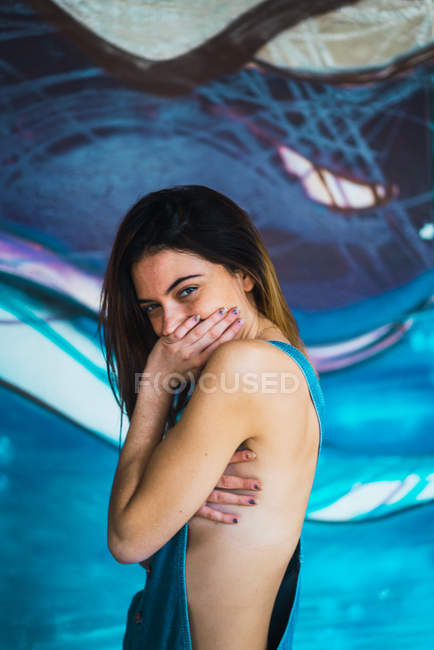 Side view of smiling brunette girl wearing overall hiding breast and smile with palms — Stock Photo