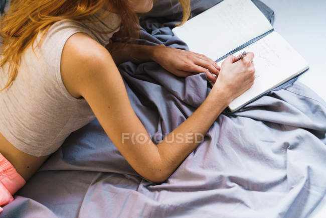 Crop girl couché sur le lit et l'écriture dans le bloc-notes — Photo de stock