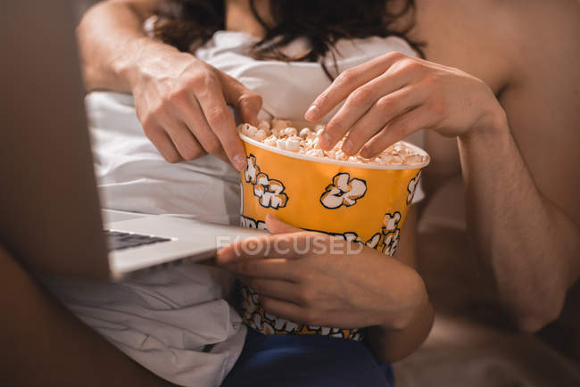 Midsection de casal que navega laptop e comer pipocas — Fotografia de Stock
