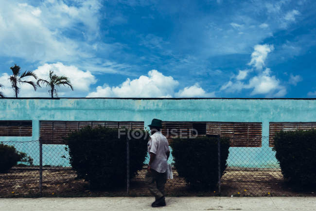 Kuba - 27. August 2016: Seitenansicht eines Mannes, der neben einem türkisfarbenen Industriegebäude spaziert. — Stockfoto