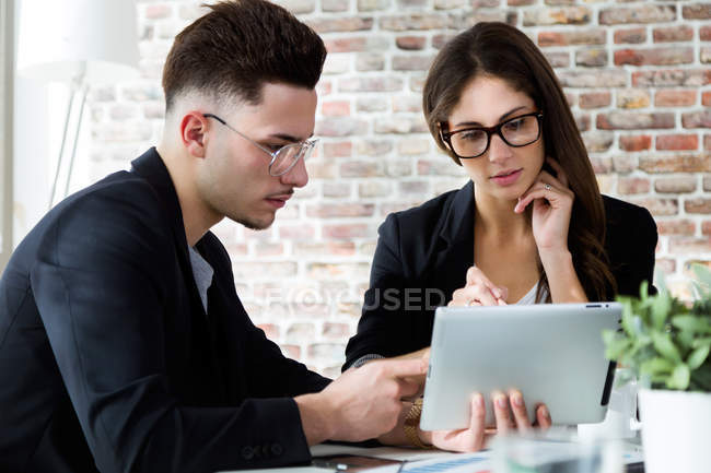 Geschäftsmann zeigt Kollege Tablet-Bildschirm, während er im Büro am Tisch sitzt — Stockfoto