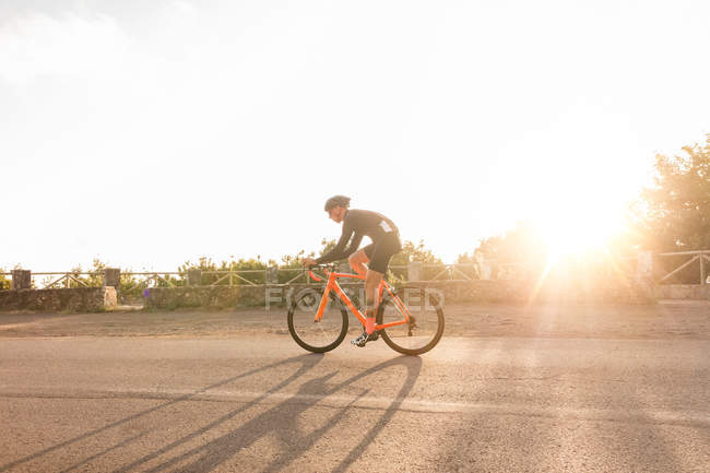 Vue latérale du cycliste à vélo sur route éclairée par le soleil en été — Photo de stock
