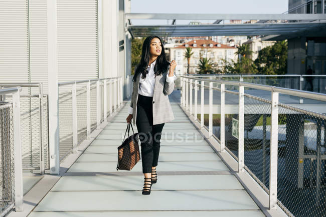 Elegante donna d'affari con borsa a piedi al passaggio balcone e guardando altrove — Foto stock