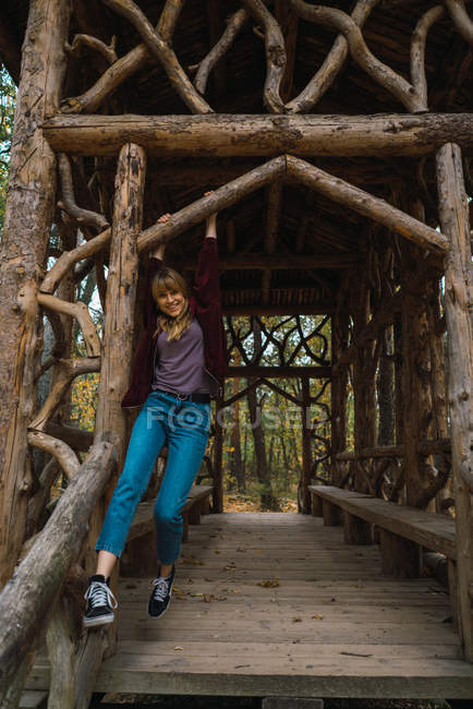 Sorridente ragazza bruna in giacca rossa con cappuccio appesa in passaggio di legno — Foto stock