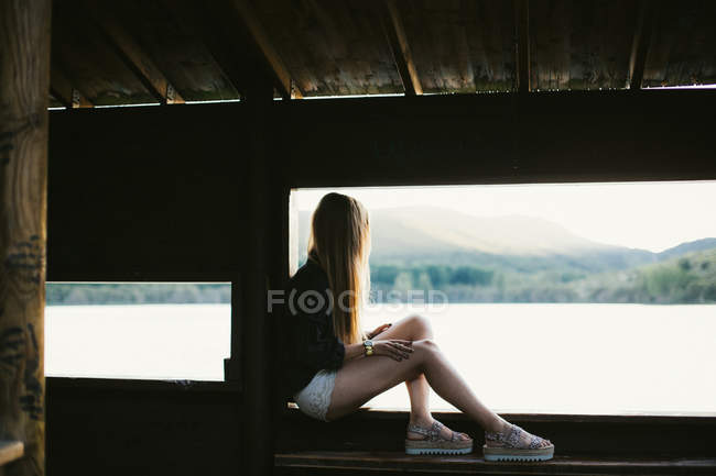 Unerkennbare Frau sitzt unter Brücke und bewundert Blick auf Fluss. — Stockfoto