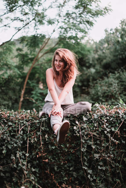 Charmante Frau sitzt auf grünem Zaun und lächelt in die Kamera. — Stockfoto