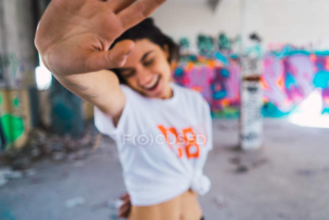 Mujer sonriente escondiéndose de la cámara. en habitación abandonada con graffiti - foto de stock
