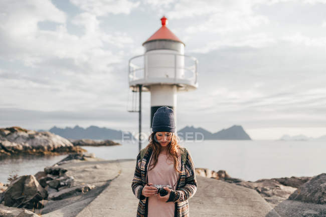 Porträt einer Frau, die mit Kamera über dem Wasserturm am Seeufer im Hintergrund steht — Stockfoto