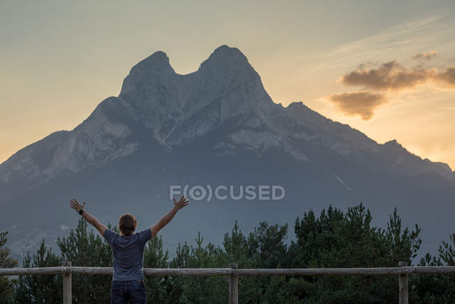 Rear view of happy man cheerfully outstretching arms aside at mountains countryside — Stock Photo