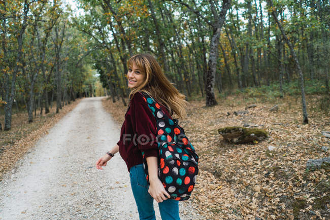Brunette fille en sweat à capuche rouge marchant sur le chemin de la forêt et regardant par-dessus l'épaule à la caméra — Photo de stock