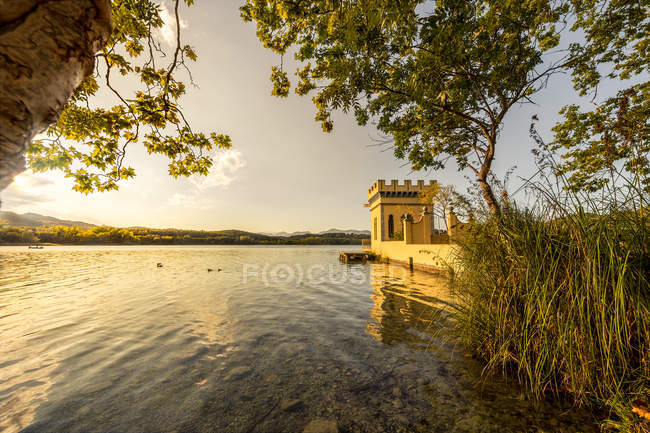 Vista cenica sulla riva del lago con torre in pietra illuminata dal sole — Foto stock