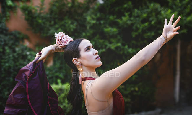 Вид сбоку танцовщицы фламенко с цветочком на голове, позирующей на уличной сцене — стоковое фото
