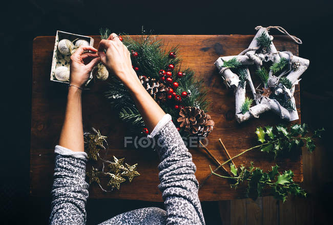 Vista superior de manos femeninas confeccionando corona de Navidad en mesa de madera - foto de stock