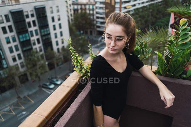 Vue à angle bas de la fille brune en lunettes posant sur la terrasse et regardant loin — Photo de stock