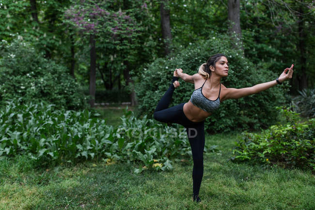 Menina atlética realizando ioga asana no gramado no parque — Fotografia de Stock
