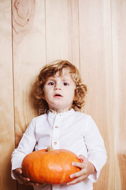 Confident child posing with pumpkin at wooden backdrop — Stock Photo